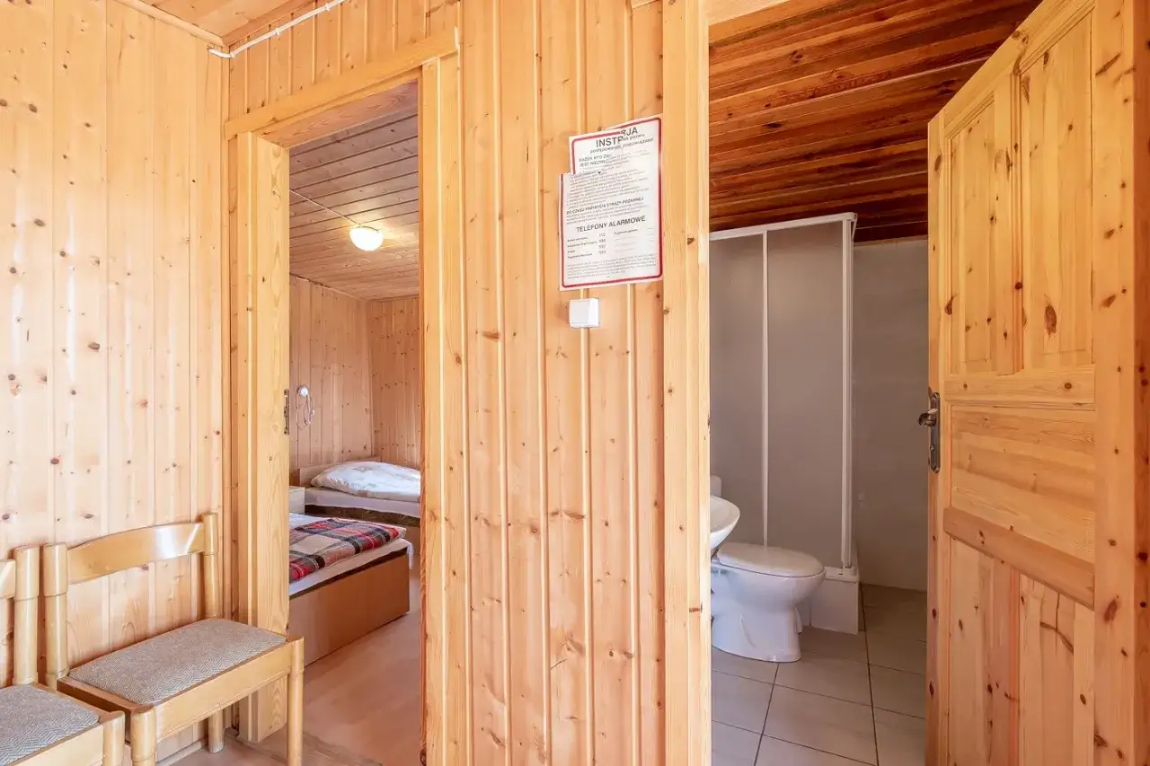 Drewniane wnętrze pokoju w ośrodku wczasowym Janina. Widok na łóżka, łazienkę z prysznicem i toaletą.