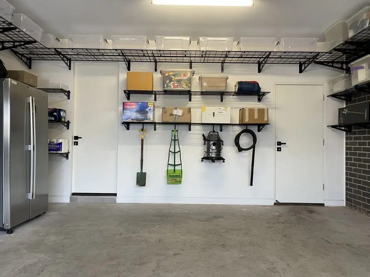 Zorganizowany garaż z lodówką, półkami pełnymi pudeł i pojemników. Warto wiedzieć, ile kosztuje wynajem garażu, by móc tak przechowywać rzeczy.