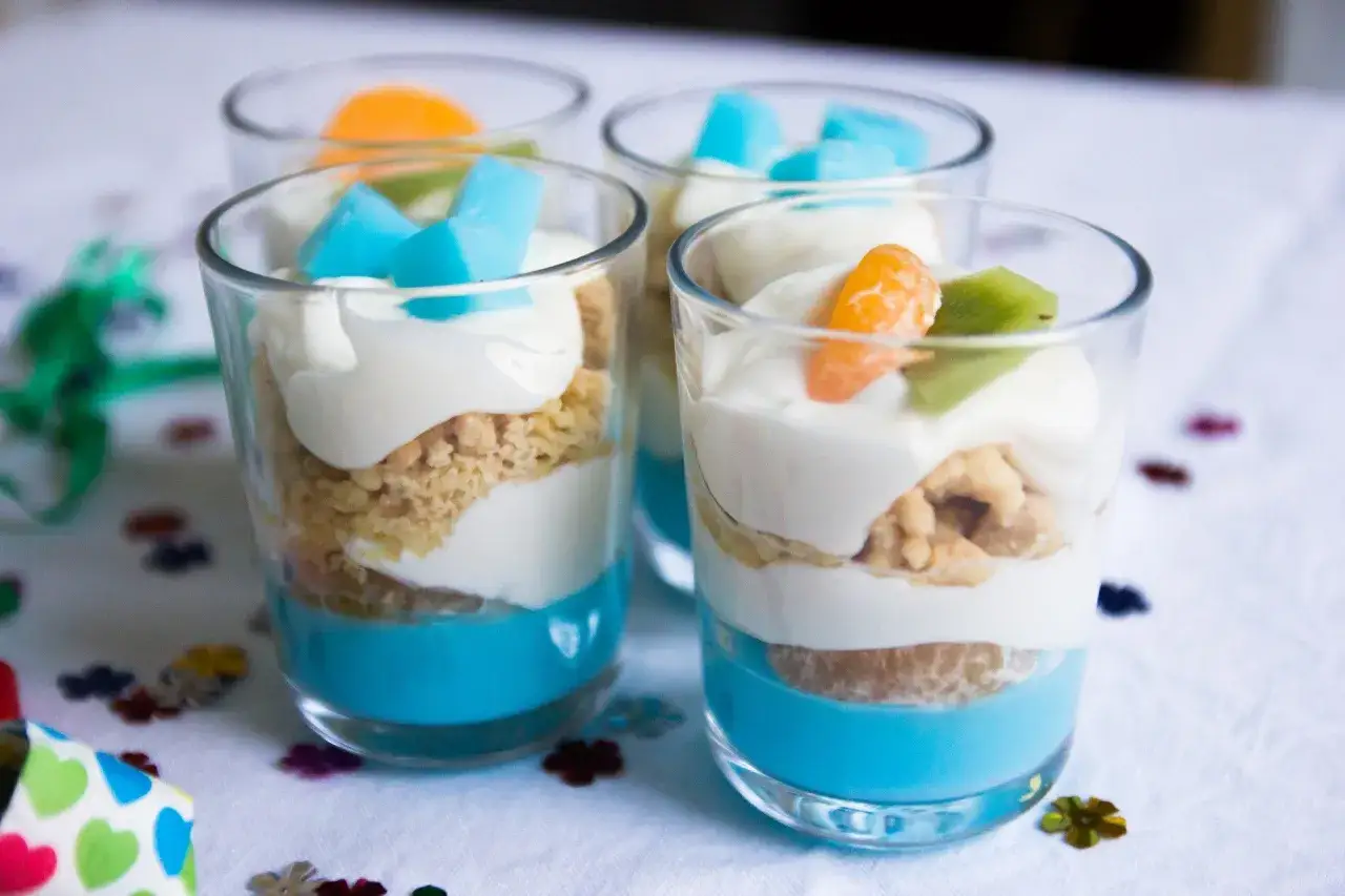 Kolorowe mini deserki z galaretką, jogurtem i owocami, idealne na przyjęcie.