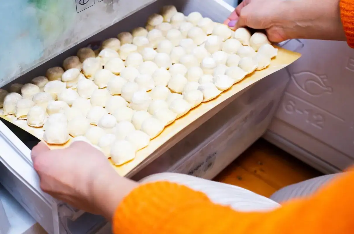 Rządki surowych pierogów na tacce trafiają do zamrażarki. Tak wygląda proces, jak mrozić pierogi, by cieszyć się nimi później.