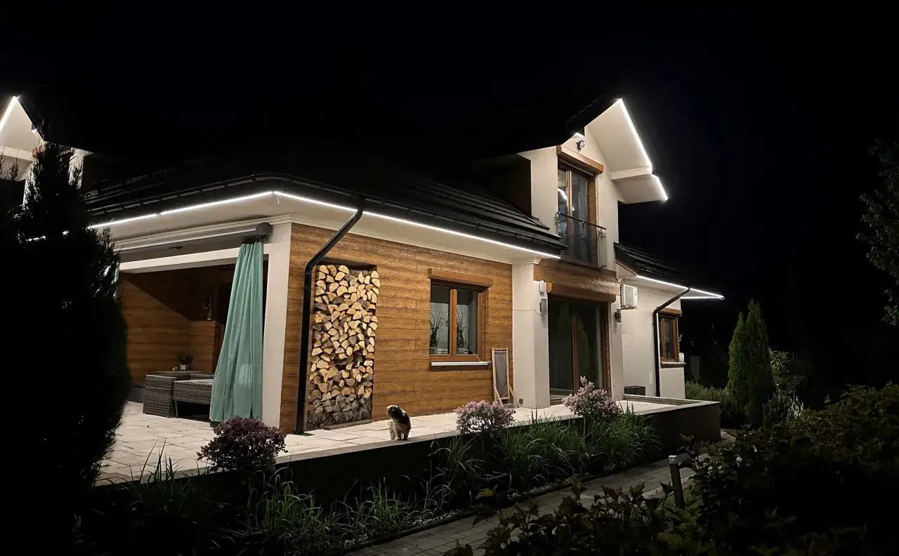 Nowoczesne oświetlenie elewacji domu parterowego podkreśla drewniane detale i tworzy przytulną atmosferę.