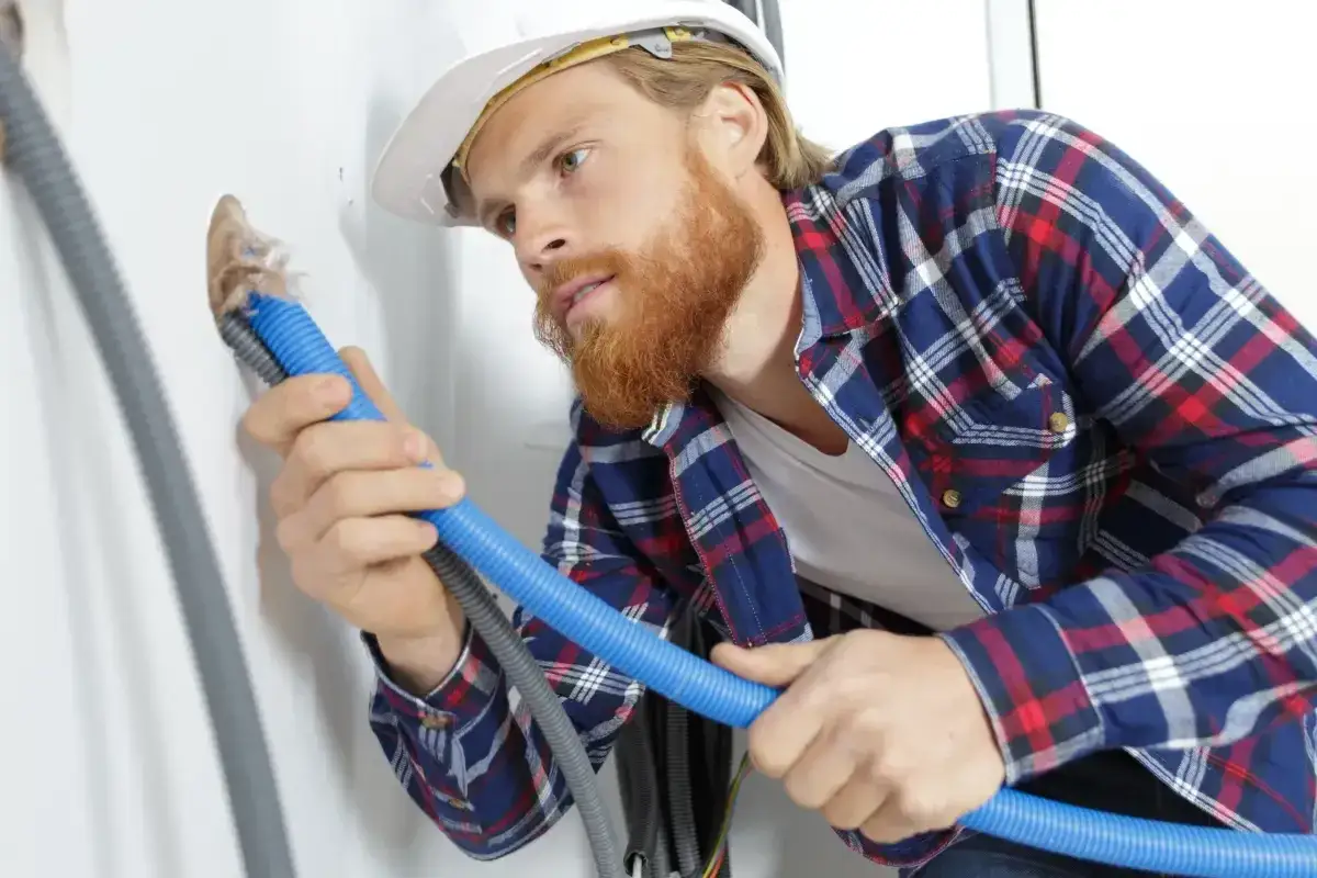 Budowlaniec w kasku wykonuje uszczelnienie przejścia rury przez ścianę, dbając o dokładność pracy.