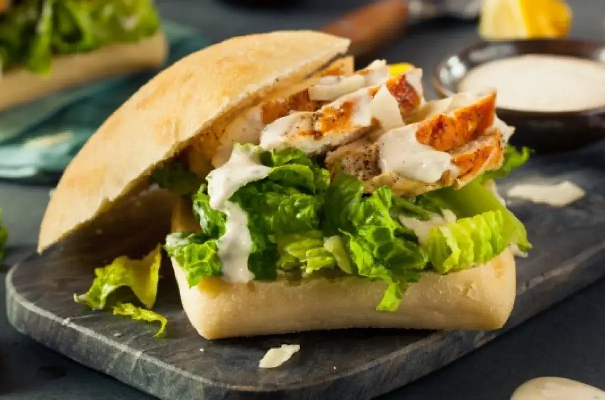 Pyszna kanapka z kurczakiem, świeżą sałatą i kremowym sosem, podana na desce.