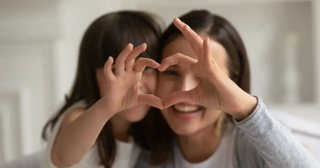 Kobieta i dziecko tworzą serce dłońmi, symbolizując miłość i gotowość do tego, jak adoptować dziecko.