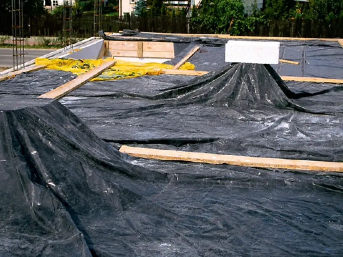 Czarna folia zabezpiecza świeży strop przed wilgocią. Drewniane deski i żółta membrana wskazują na etapy budowy.