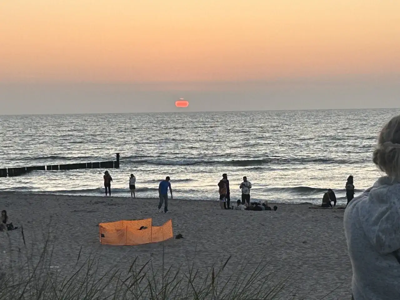 Zachód słońca nad morzem w Mielnie. Ludzie spacerują po plaży, zastanawiając się, ile mieszkańców ma Mielno.