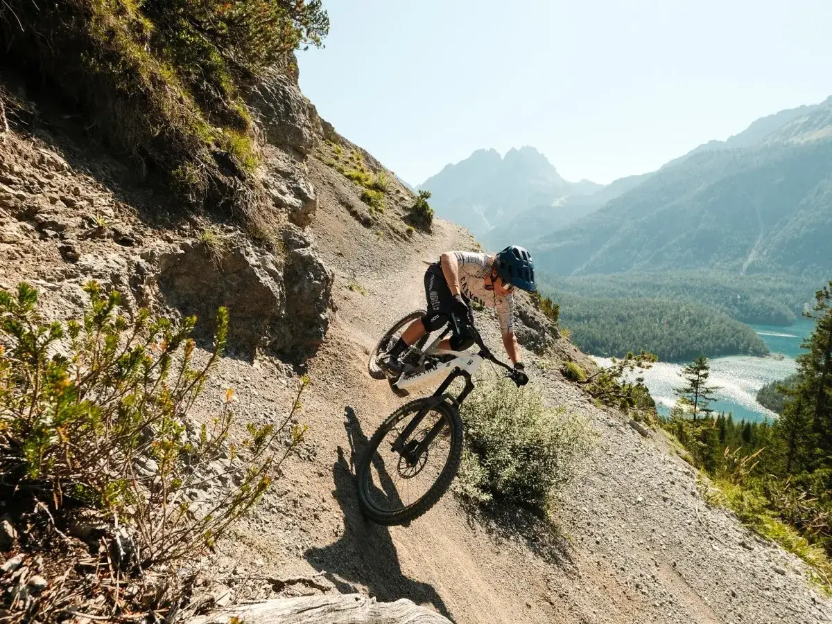 Rowerzysta zjeżdża po kamienistym szlaku, pokazując, czym jest **enduro co to** za sport. Widok na góry i jezioro zapiera dech.
