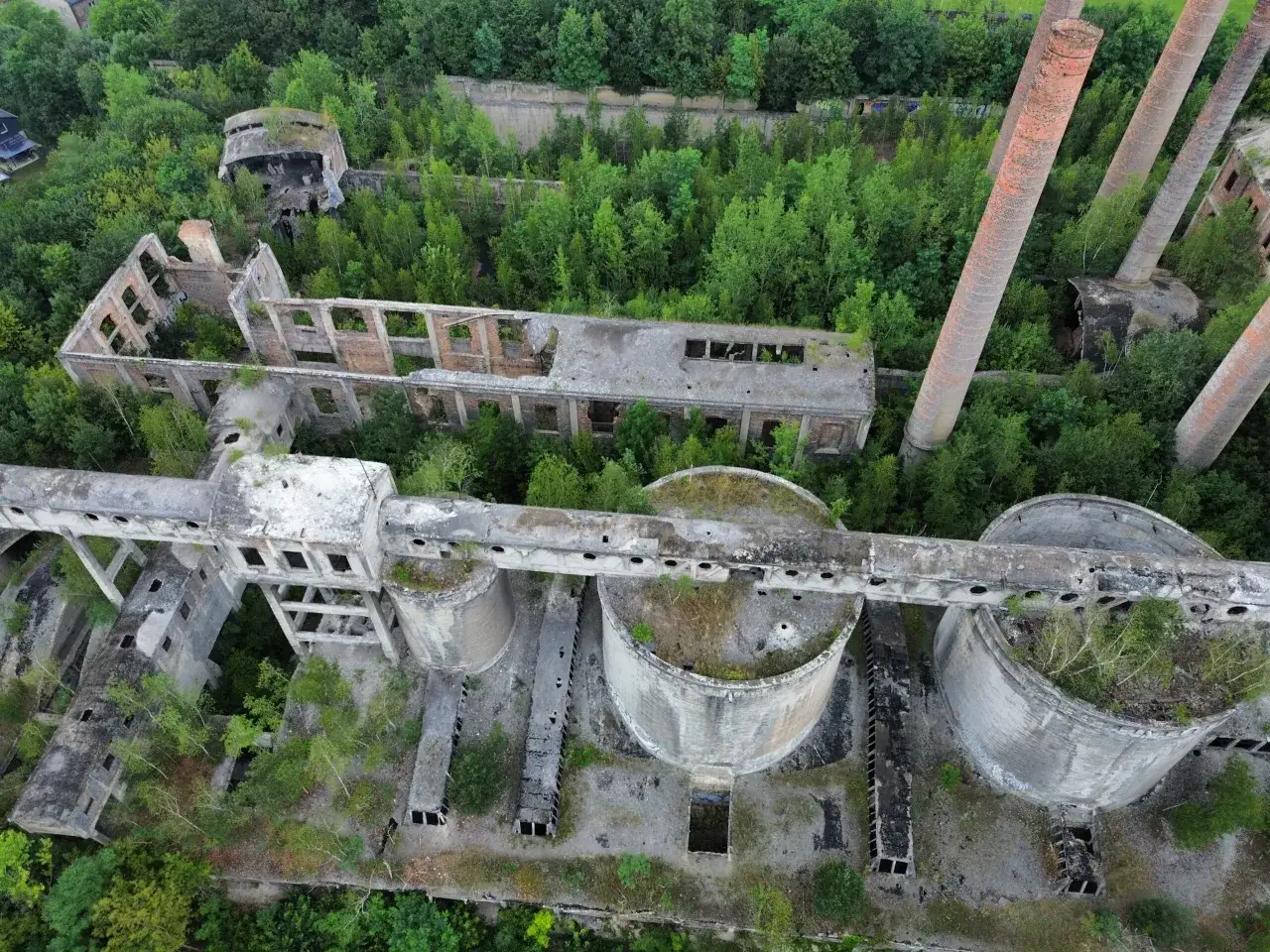 Opuszczona cementownia, gdzie kiedyś wynaleziono cement, porośnięta zielenią. Ruiny budynków, silosy i wysokie kominy.