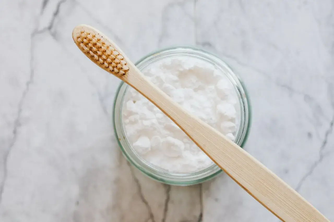 Drewniana szczoteczka do zęb&oacute;w leży na słoiku z białym proszkiem, kt&oacute;ry może pom&oacute;c w walce z kamieniem na zębach.