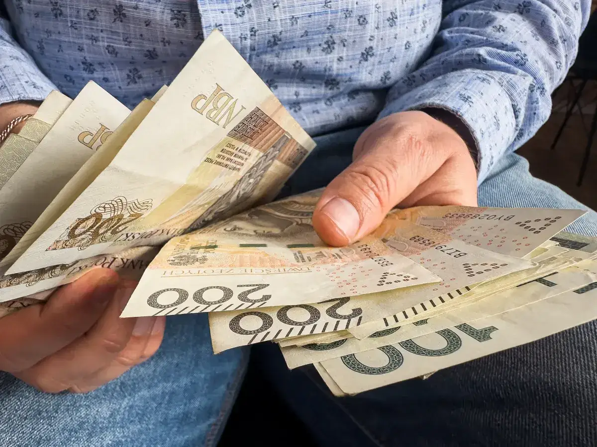 Dłonie trzymające polskie banknoty 200 zł i 100 zł. Zastanawiasz się, czy świadczenie socjalne wlicza się do dochodu?
