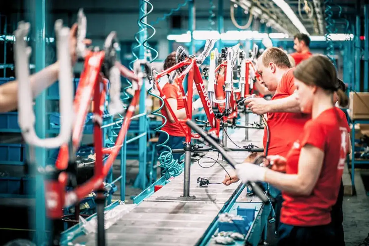 Pracownicy w fabryce rower&oacute;w składają czerwone ramy rowerowe.
