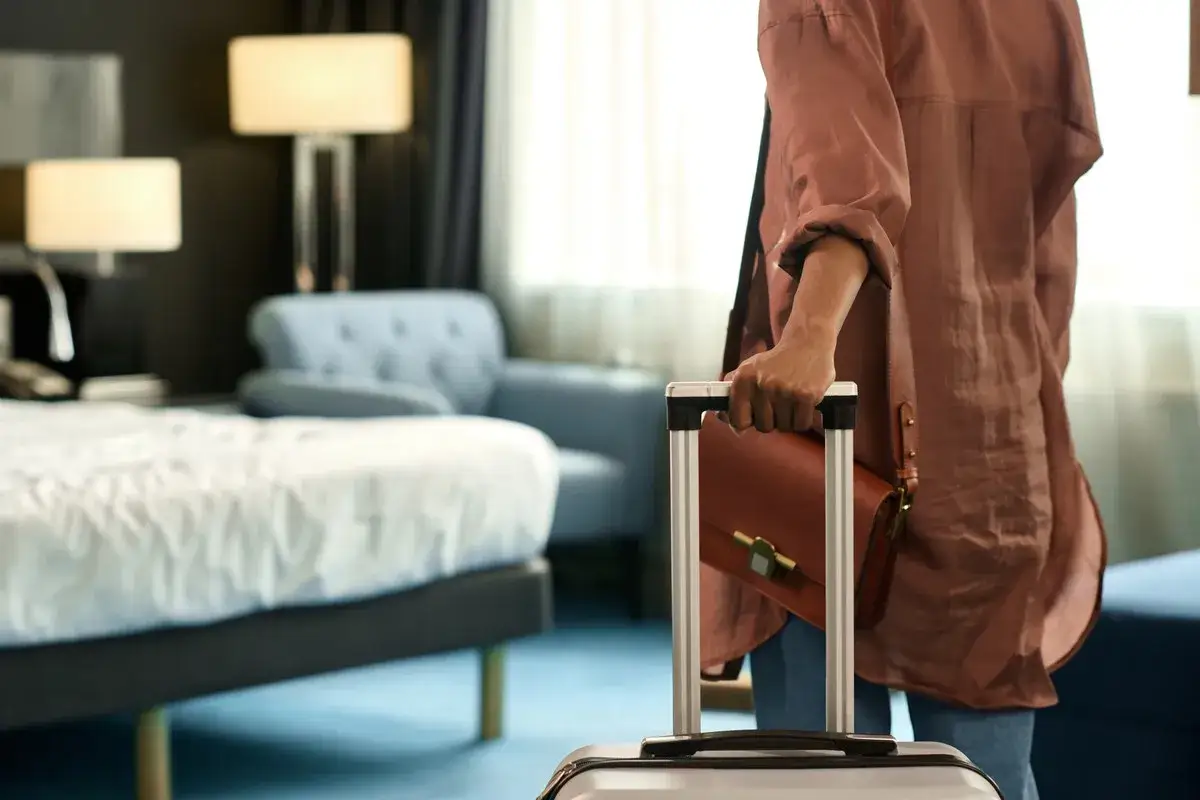 Osoba z walizką i brązową torebką w pokoju hotelowym. Zastanawiasz się, co zabrać do sanatorium?