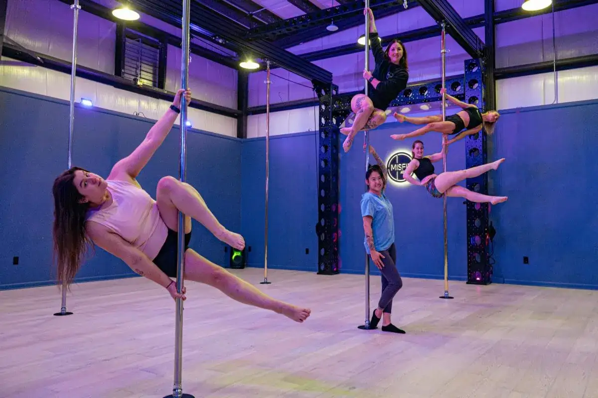 Kobiety ćwiczą na pionowych rurkach, pokazując siłę i gibkość. Czy pole dance to sport? Zdecydowanie tak, wymaga ogromnej sprawności!