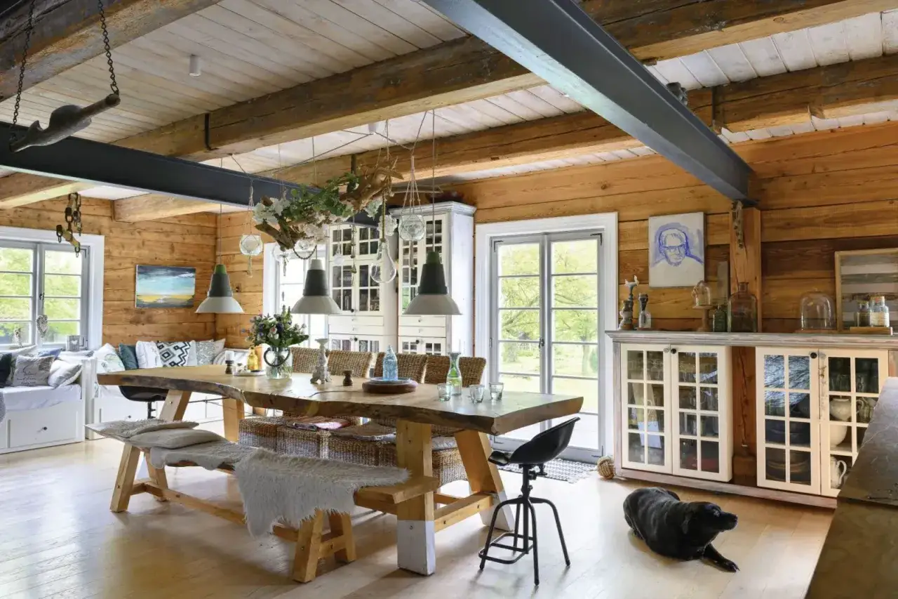 Przytulna jadalnia z drewnianym sufitem z belkami, dużym stołem i czarnym psem wylegującym się na podłodze.