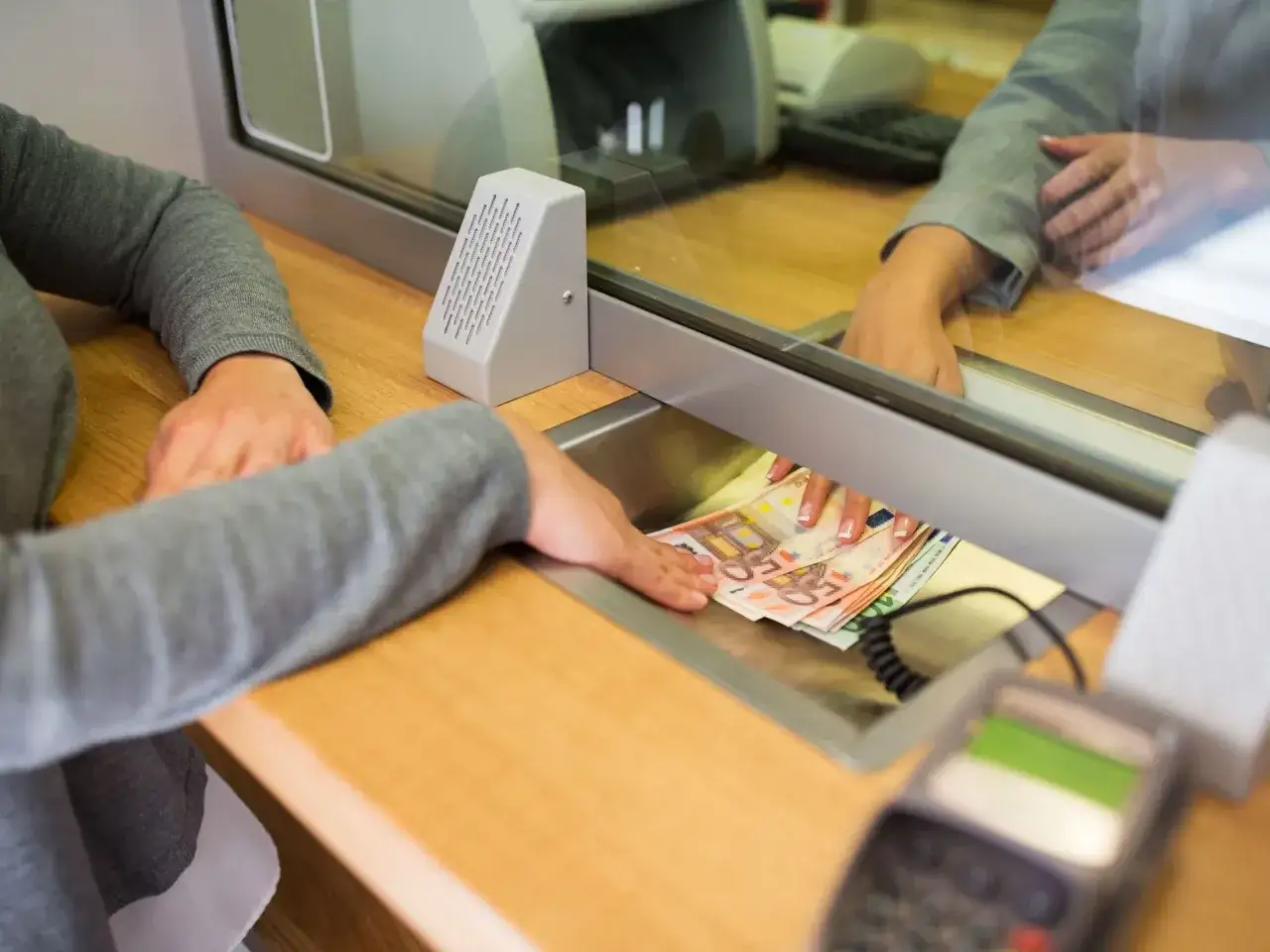 Ręce przekazują sobie banknoty euro przez szybę. Czy walutomat jest bezpieczny? Transakcja w kantorze.