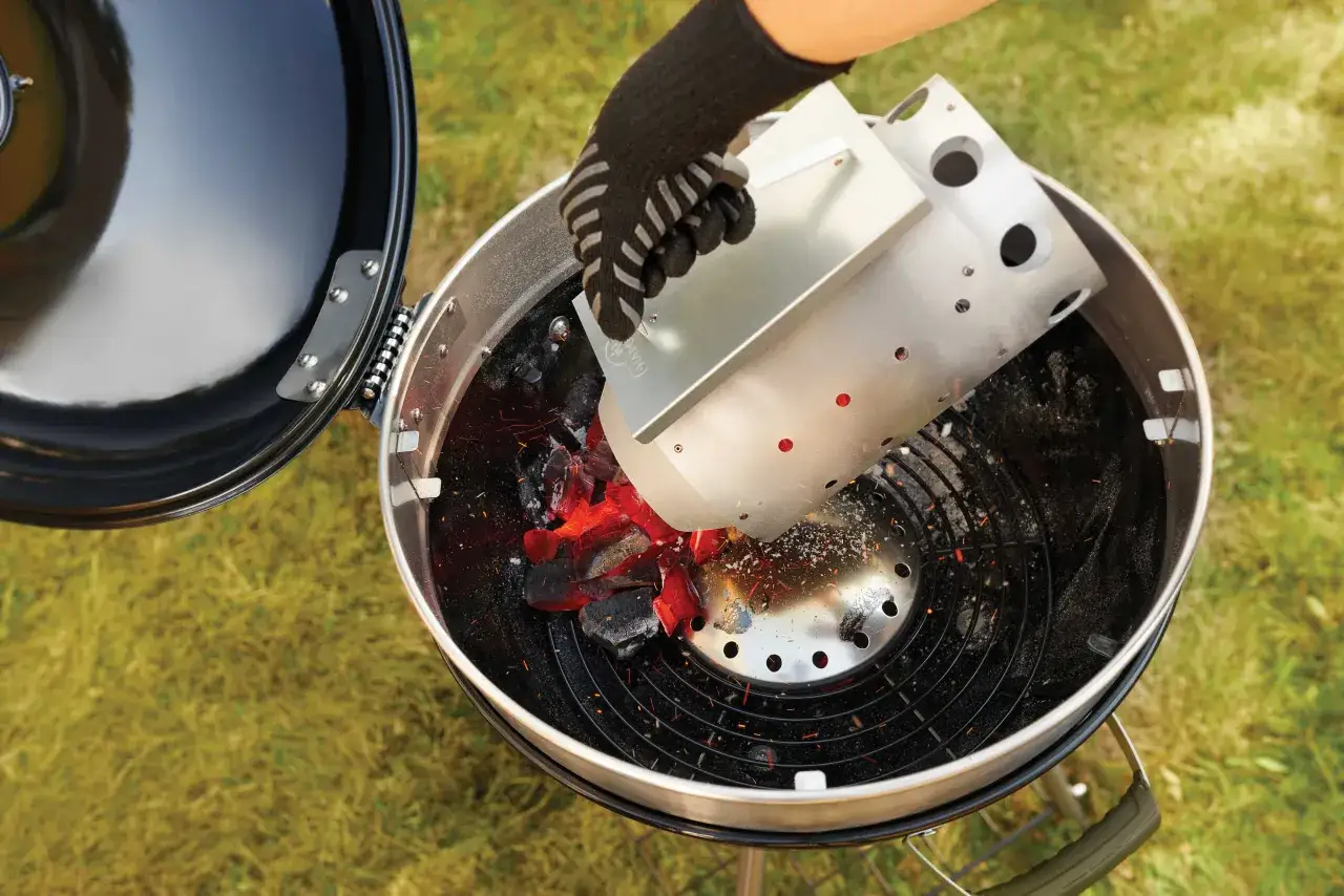 Rękawica zrzuca rozżarzone węgle do grilla, pokazując, jak rozpalac grila.