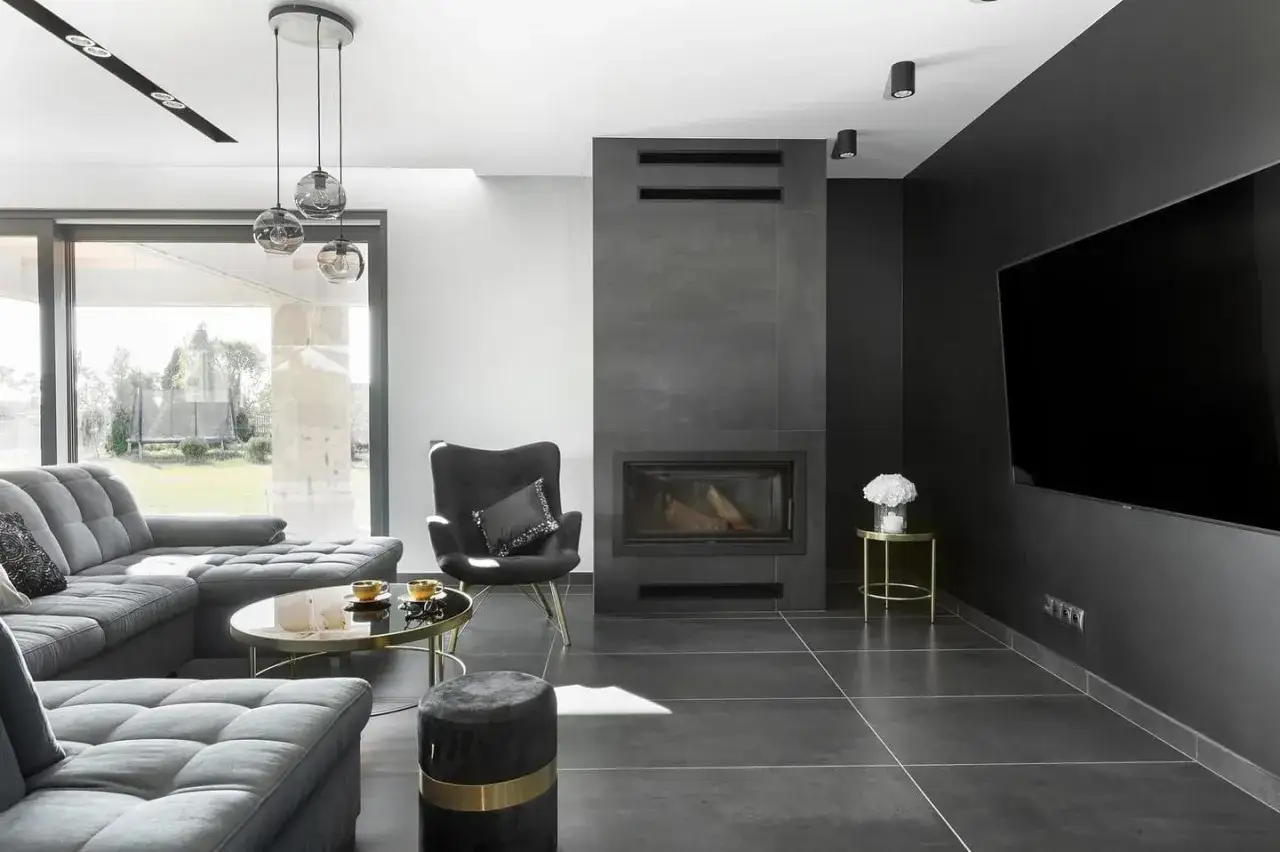 Nowoczesny salon z szarym narożnikiem, czarnym fotelem i imponującym kominkiem w salonie.