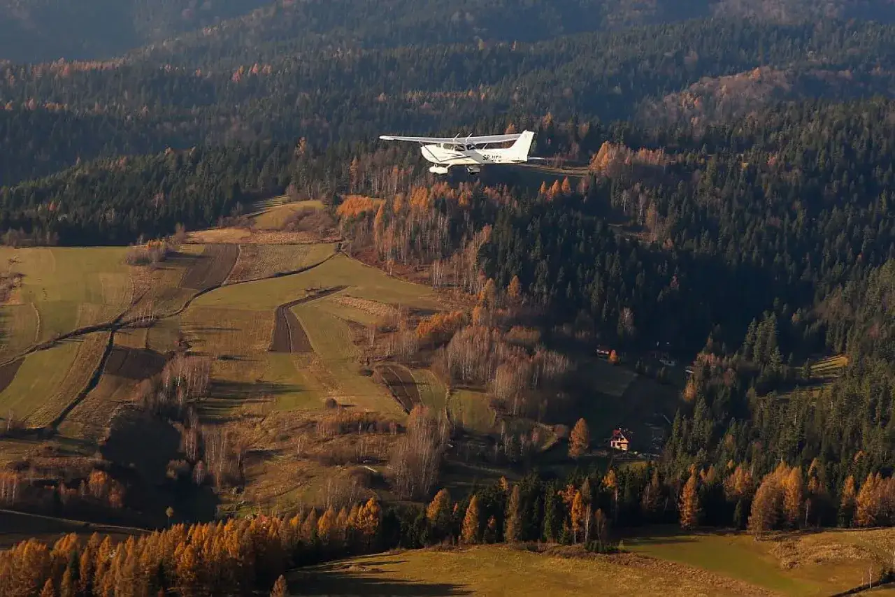 Widok na jesienne Tatry z samolotu. Mała awionetka przelatuje nad lasami i polami.