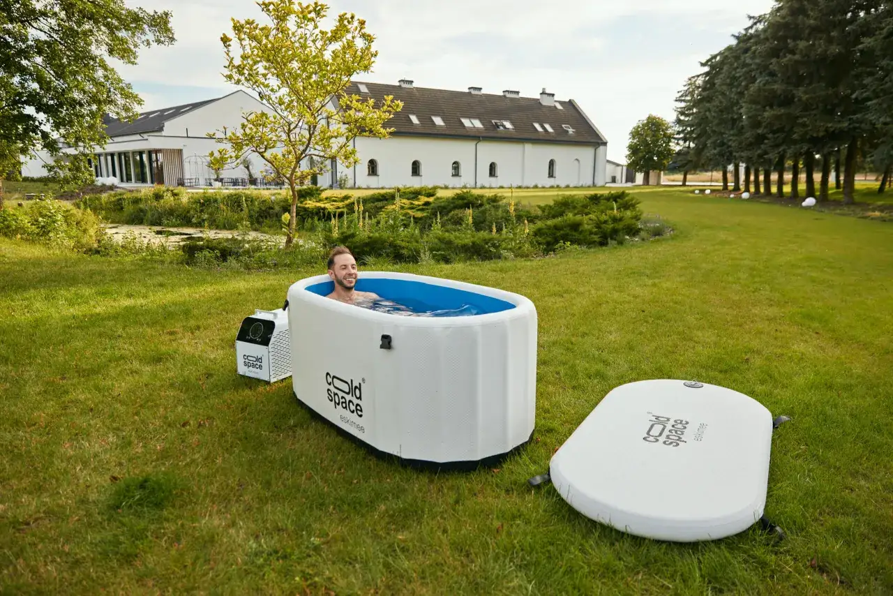 Uśmiechnięty mężczyzna w wannie z zimną wodą na trawniku, jakby czerpał z metody Wim Hof Polska.