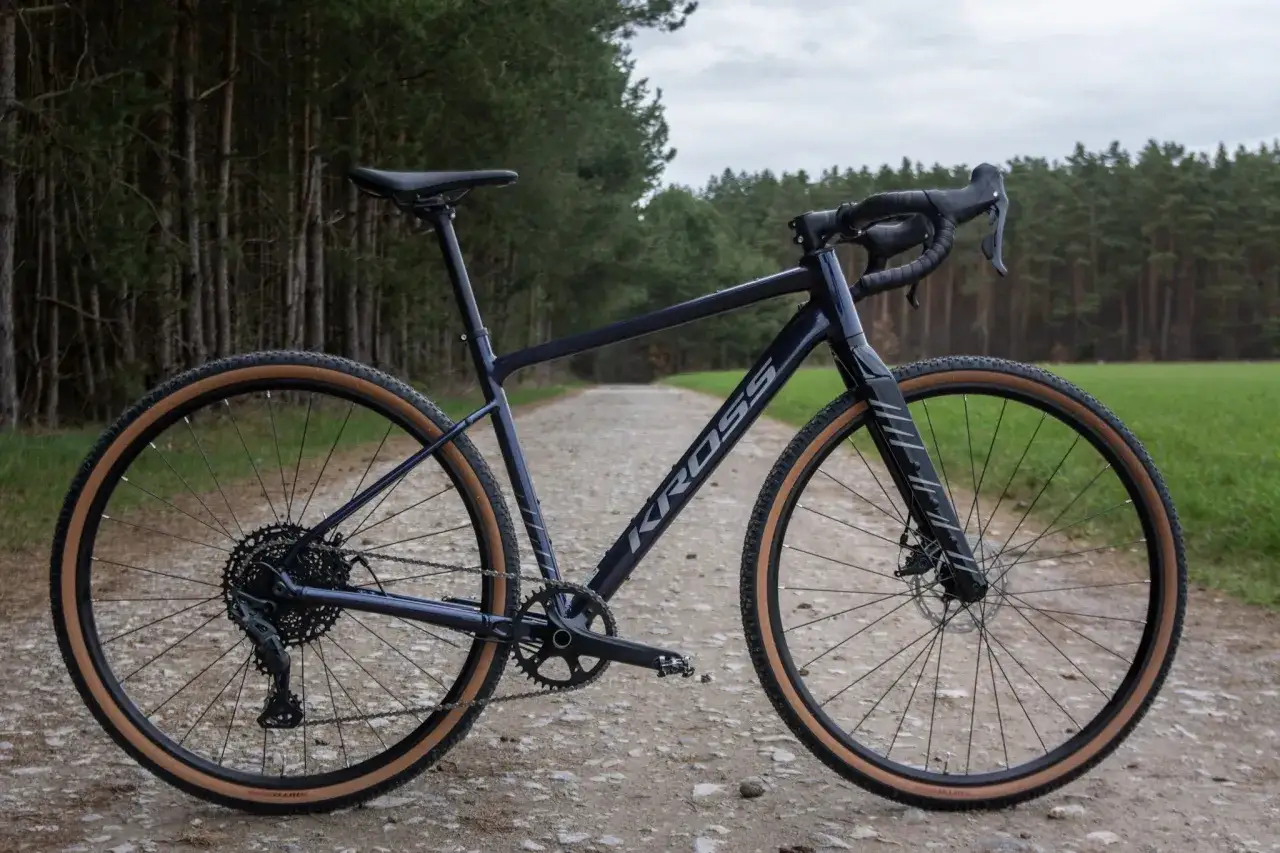 Gravelowy Kross Esker 2.0 Gen 2 na szutrowej drodze, otoczony lasem i polem. Gotowy na przygodę.