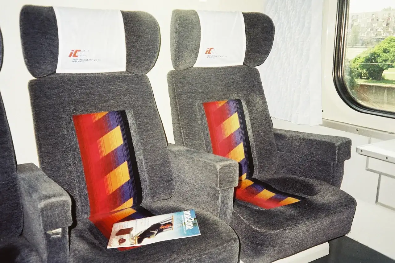 Wygodne fotele w pociągu PKP Intercity, gdzie TLK to jedna z kategorii pociągów. Na siedzeniu leży magazyn.