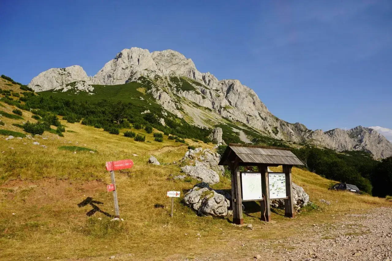 Majestatyczne g&oacute;ry w Bułgarii, zielone zbocza i skaliste szczyty. Tablica informacyjna i czerwone drogowskazy zapraszają na szlak.
