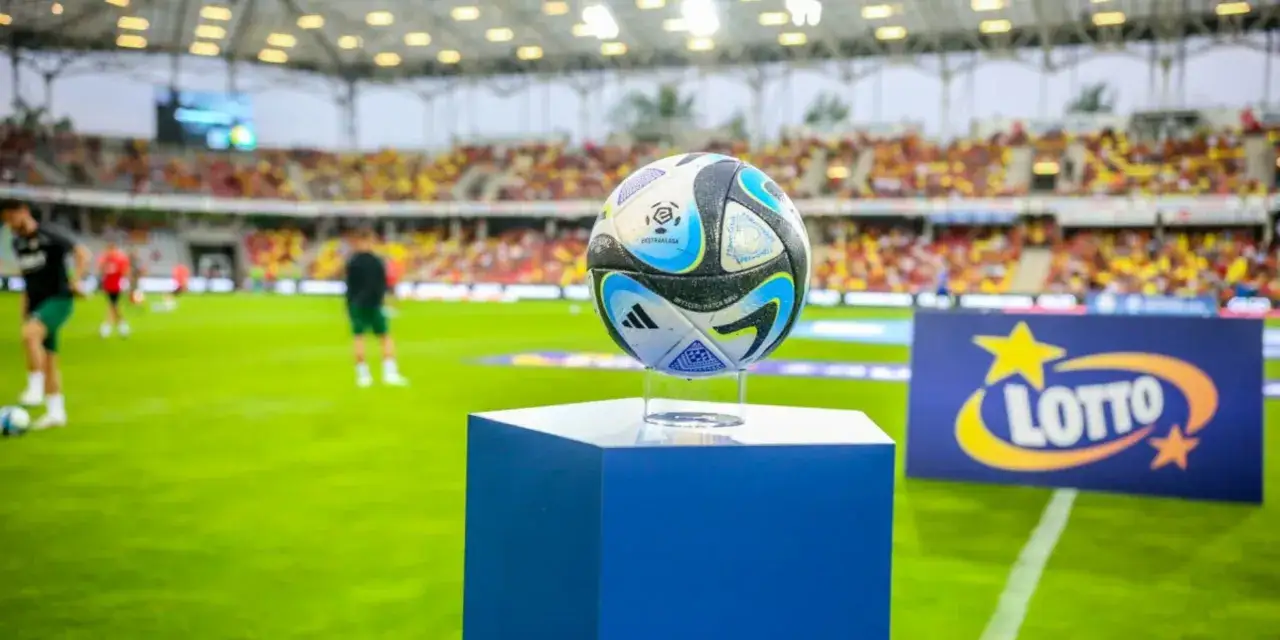Piłka do gry na niebieskim postumencie, na tle stadionu i reklamy LOTTO. Kibice na trybunach czekają na rozstrzygnięcie, ile kolejek do końca ekstraklasy.