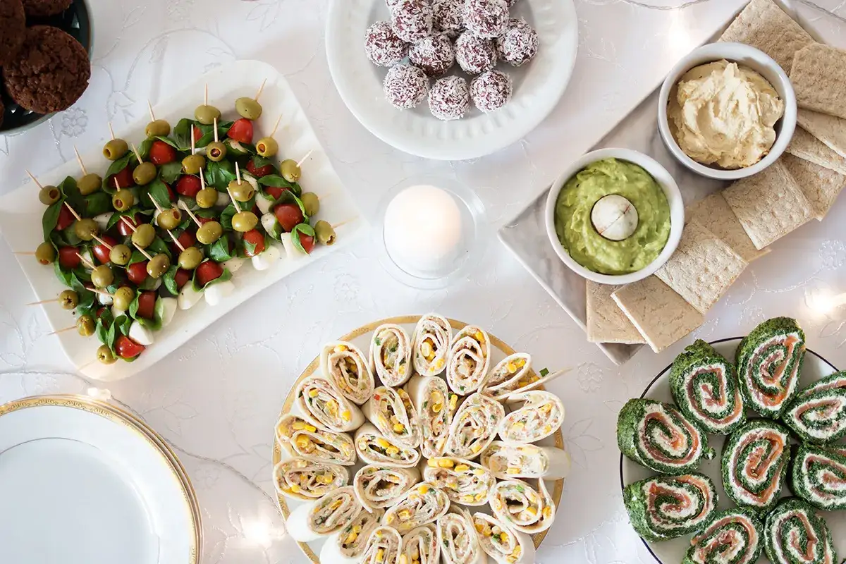 Pyszne przekąski na urodziny: koreczki caprese, roladki z łososiem i szpinakiem, tortille z kurczakiem i kukurydzą, guacamole, hummus i ciasteczka.