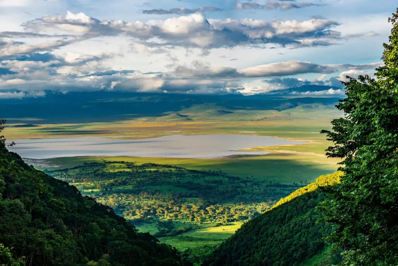 Rozległy Ngorongoro Crater z jeziorem i zielonymi wzgórzami, oświetlony słońcem przebijającym przez chmury.