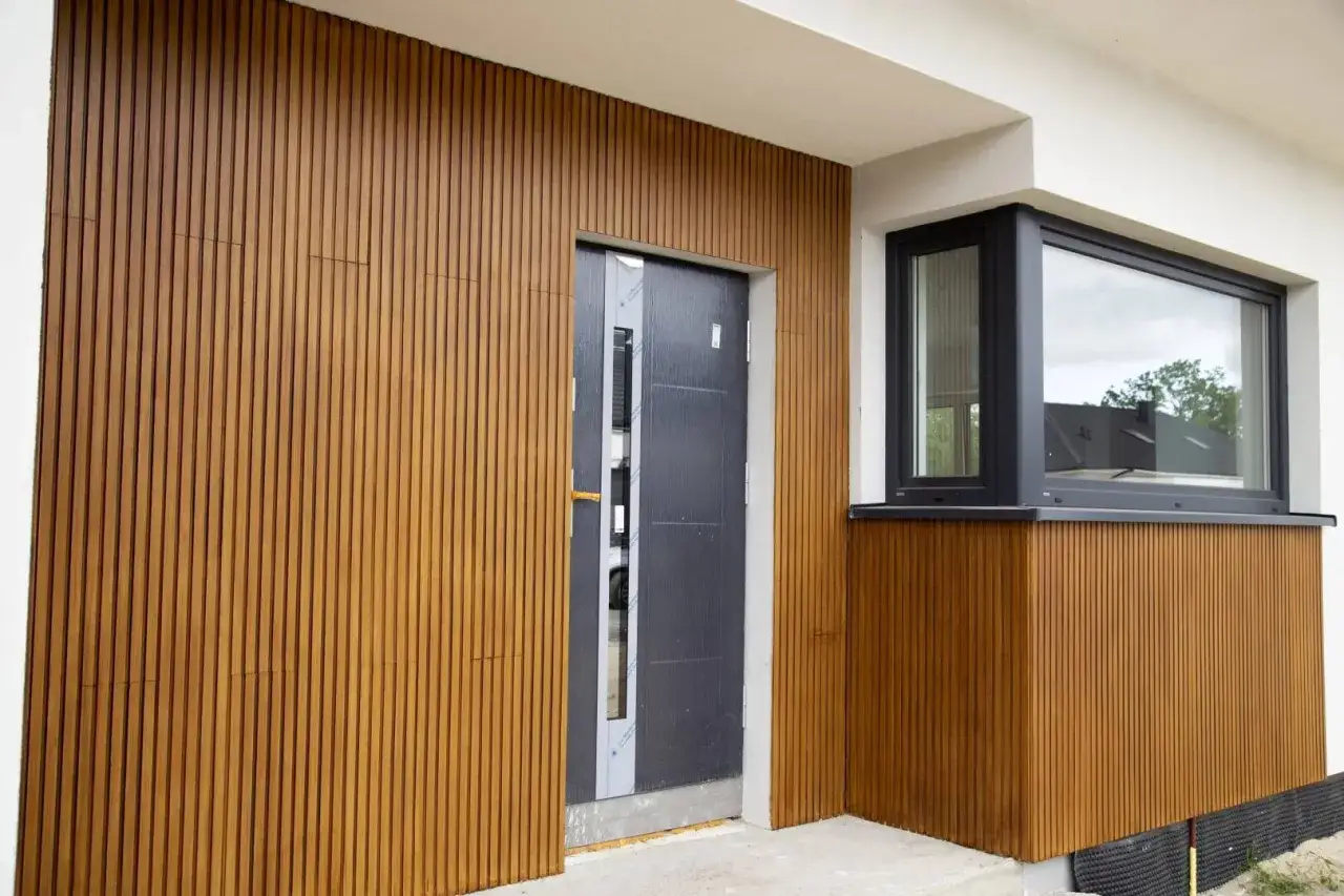 Eleganckie lamele zewnętrzne pionowe zdobią fasadę domu, otaczając nowoczesne drzwi i okno.