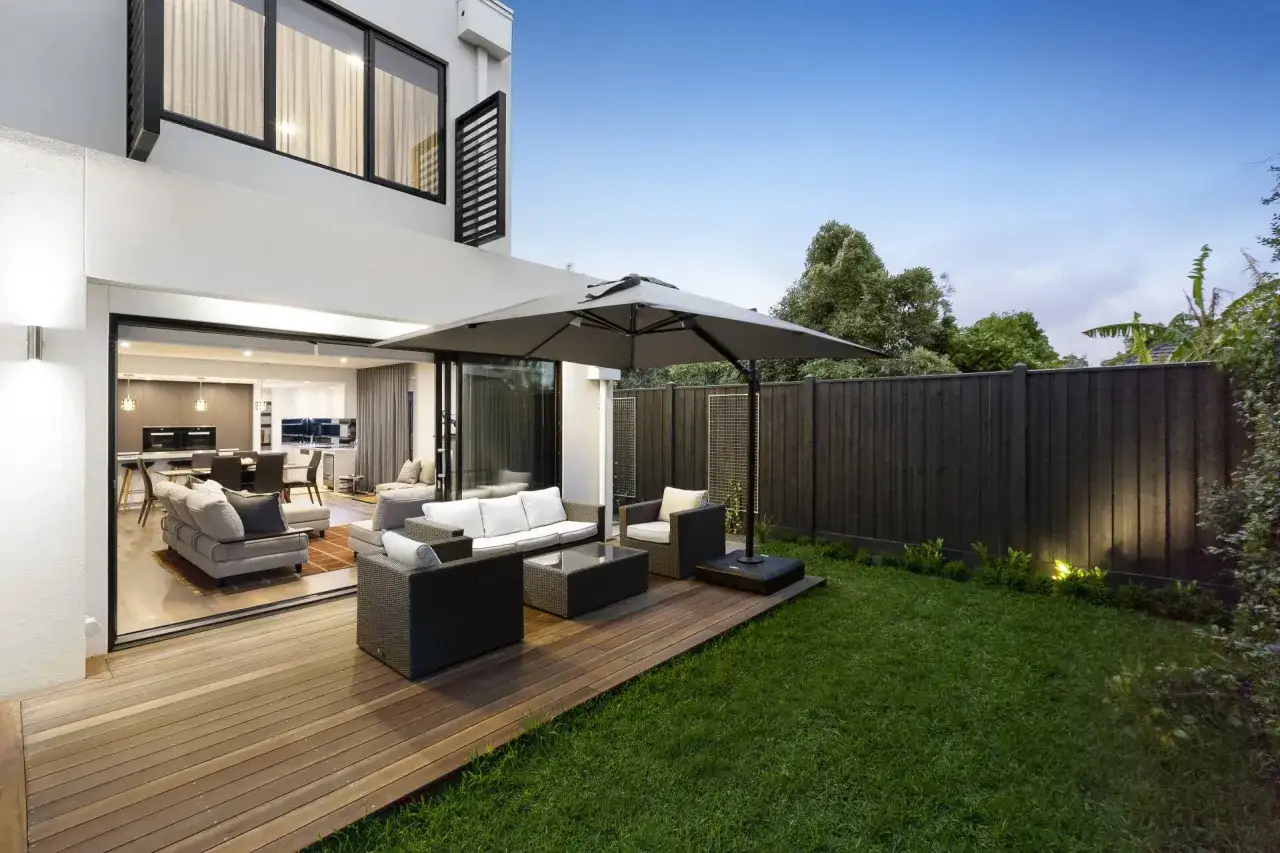 Drewniany taras z meblami ogrodowymi i parasolem. Idealne rozwiązanie, czym wyłożyć taras tanio i stylowo.