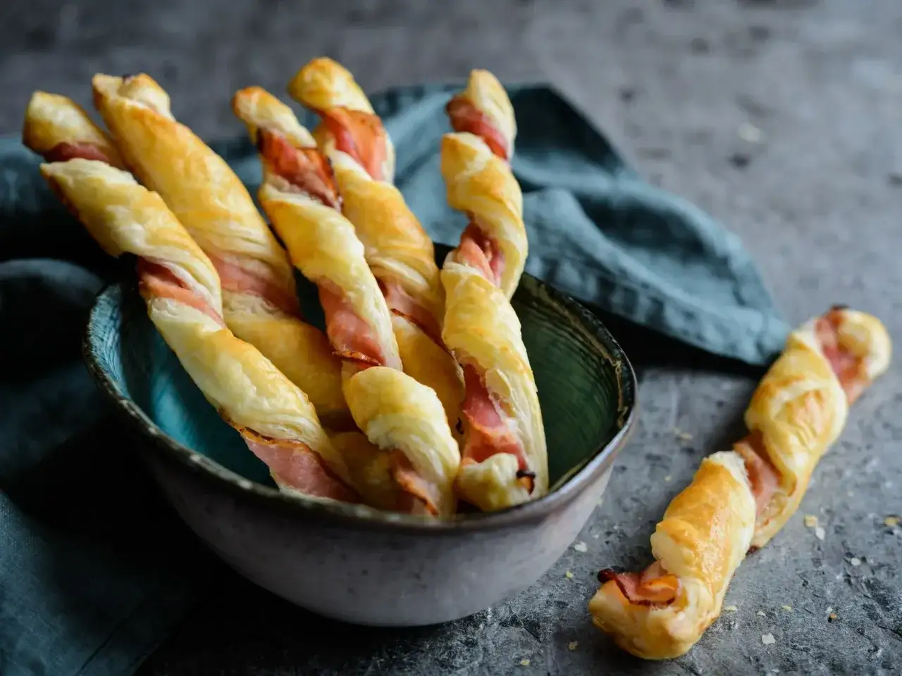 Złociste paluchy z ciasta francuskiego, zawinięte z chrupiącym boczkiem, kuszą w miseczce.