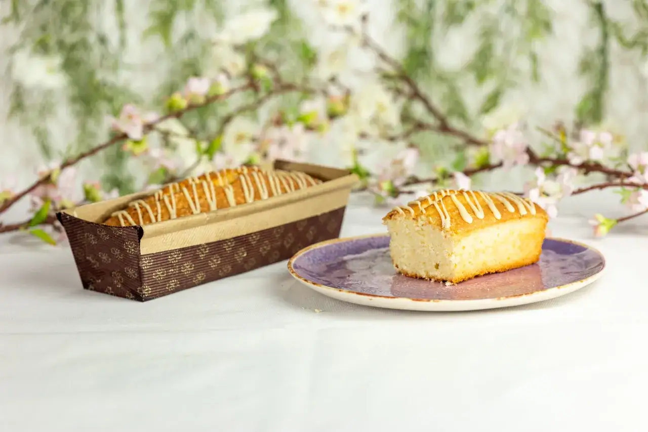 Pyszna babka piaskowa cytrynowa w papierowej formie, obok kawałek na talerzyku.