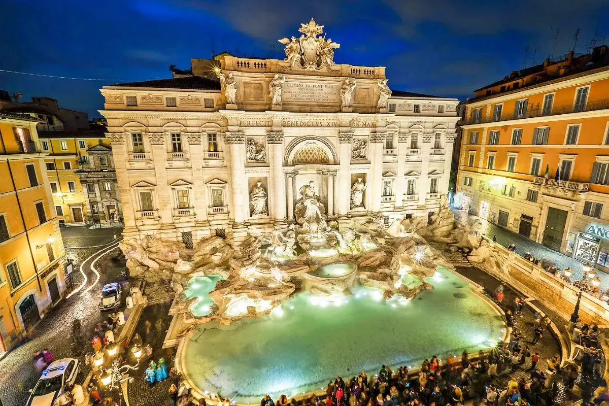 Fontanna di Trevi nocą, tłumy turyst&oacute;w i ciekawe detale architektoniczne.