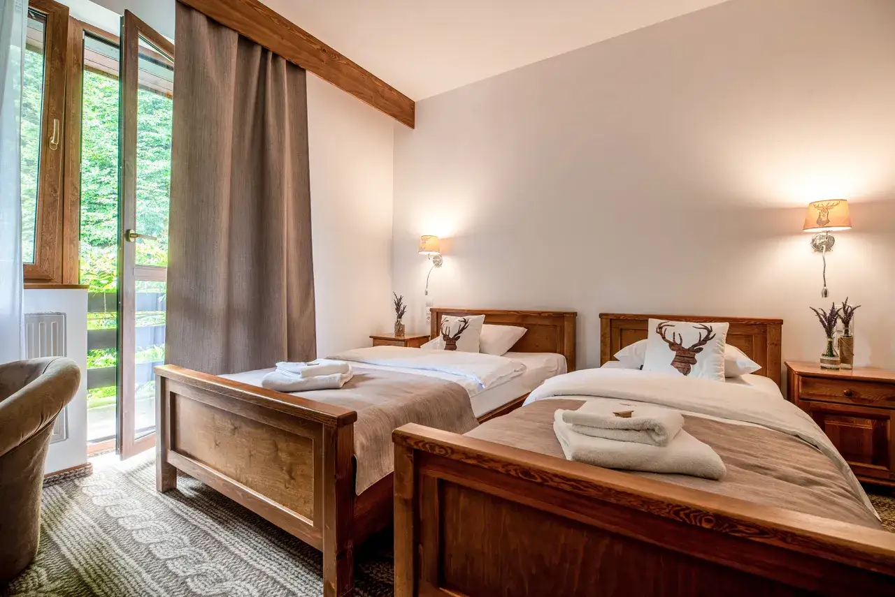 Przytulna bac&oacute;wka z dwoma ł&oacute;żkami, ozdobiona poduszką z motywem białego jelenia. Okno z widokiem na zieleń.