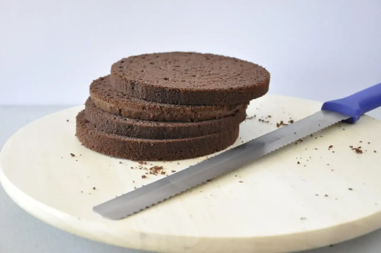 Stos ciemnych, puszystych krążk&oacute;w biszkoptu na tort, obok leży n&oacute;ż do krojenia ciasta.