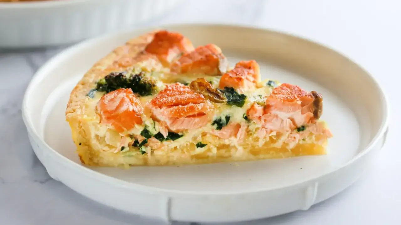Pyszna tarta z łososiem, brokułami i szpinakiem na kruchym cieście, podana na białym talerzu.