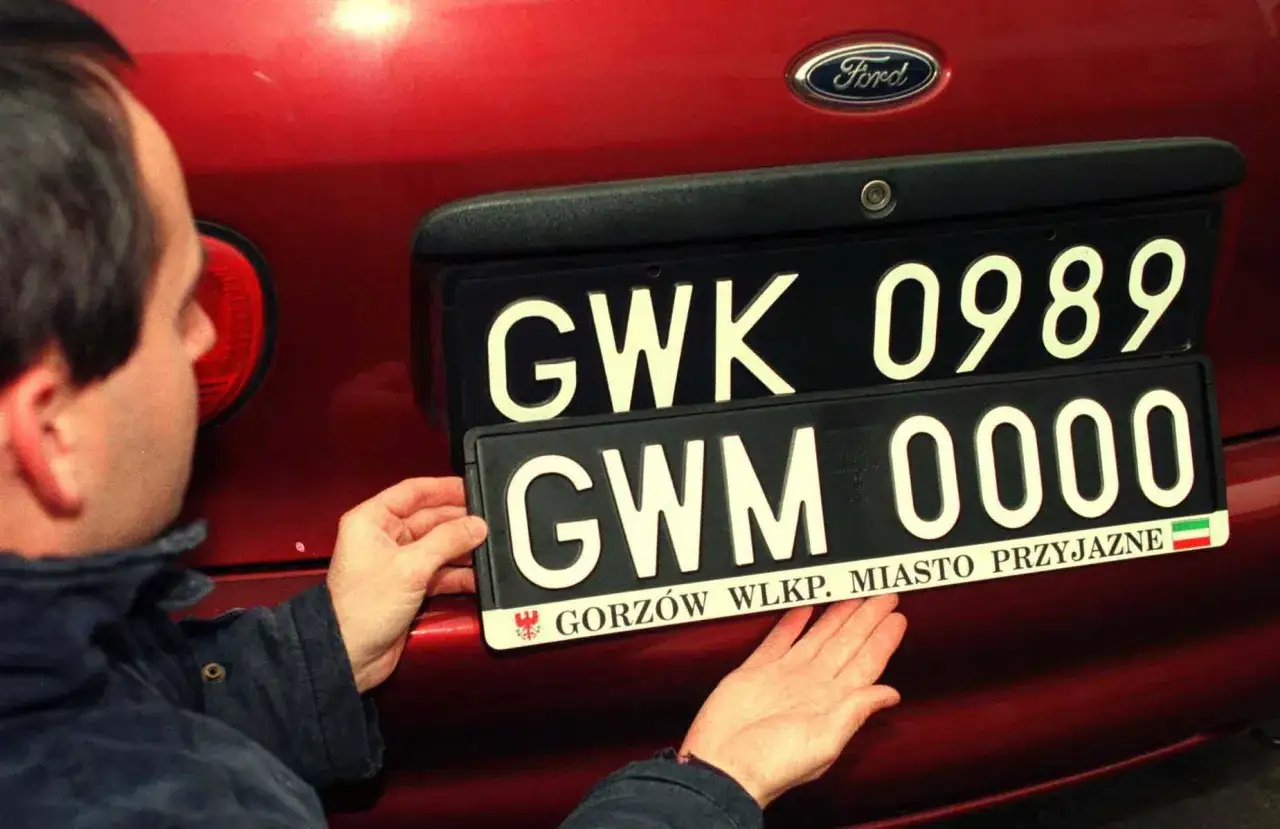 Mężczyzna montuje czarne tablice rejestracyjne z napisem 