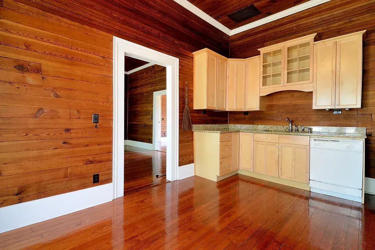 Piękny, błyszczący wykończenie boazerii w kuchni z jasnymi szafkami i widokiem na kolejne pomieszczenie.