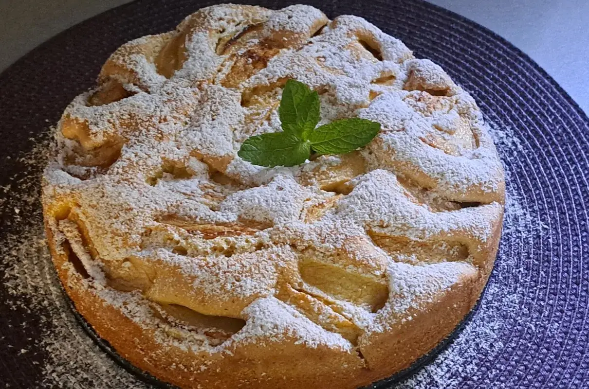 Szybki jabłecznik na oleju, posypany cukrem pudrem i udekorowany listkiem mięty, wygląda apetycznie.