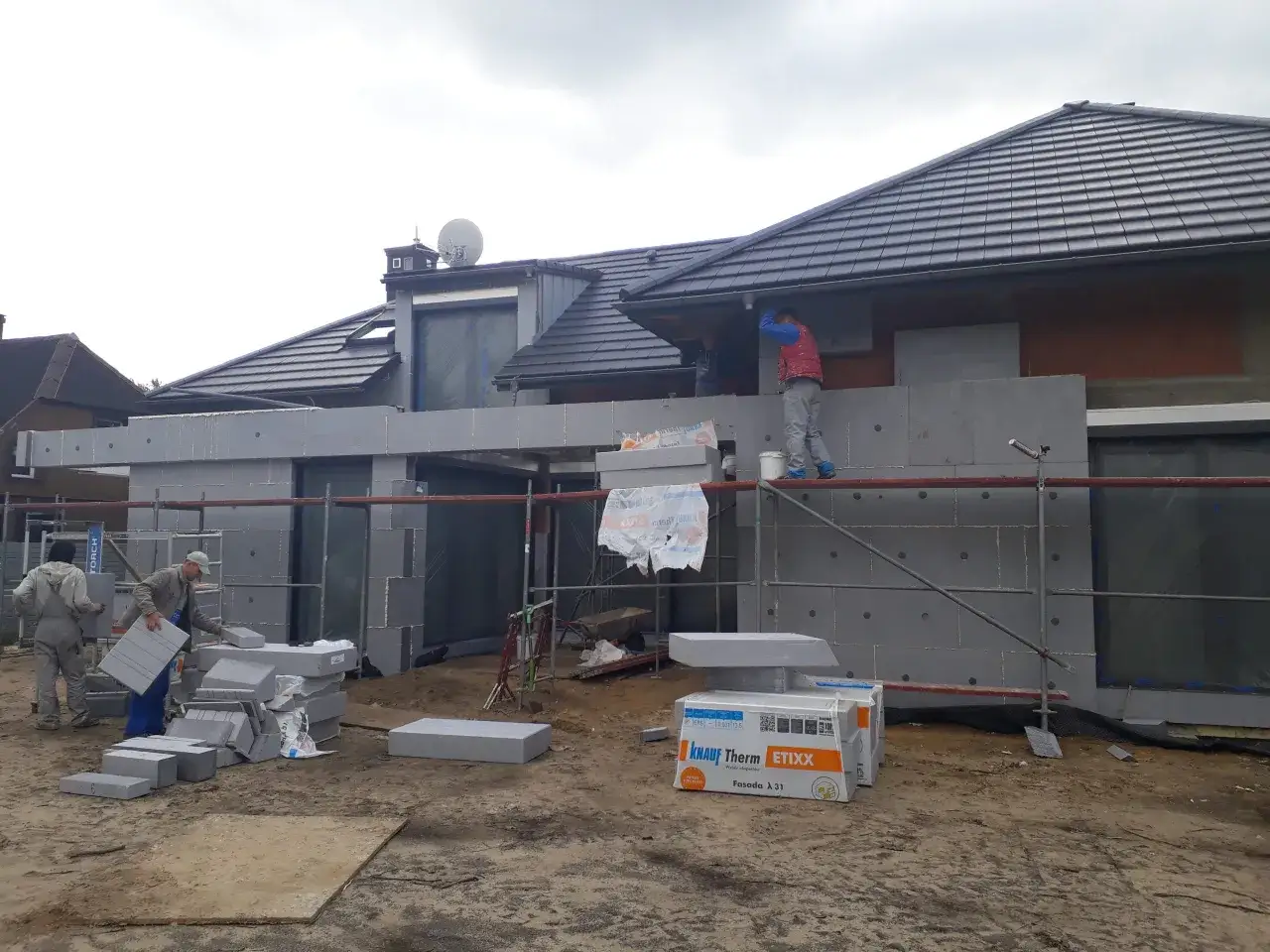 Budowa domu, pracownicy montują styropian grafitowy na elewacji. Czy trzeba kołkować styropian grafitowy? Pytanie wisi w powietrzu.