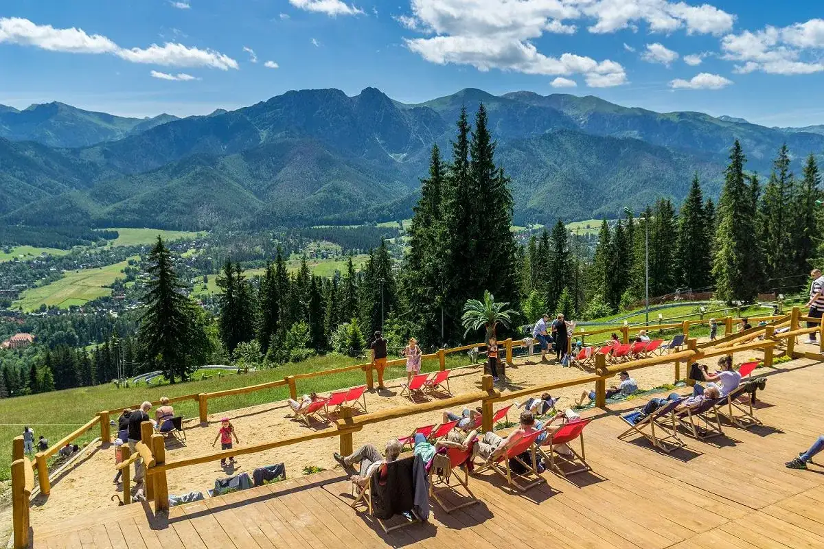 Widok na Tatry z tarasu w Zakopanem. Ludzie odpoczywają na leżakach, podziwiając piękne g&oacute;ry.