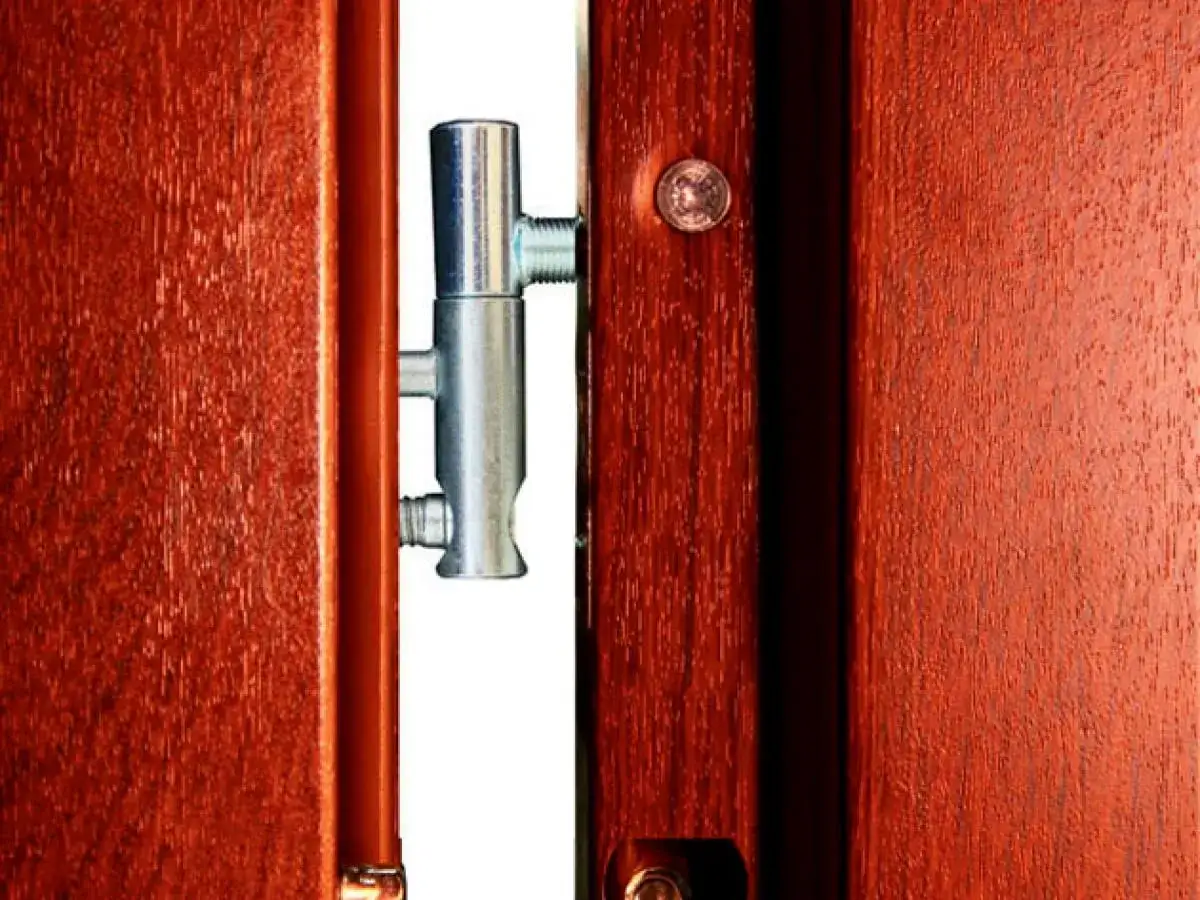 Metalowy zawias w drewnianych drzwiach, pokazujący, jak wyregulować drzwi.
