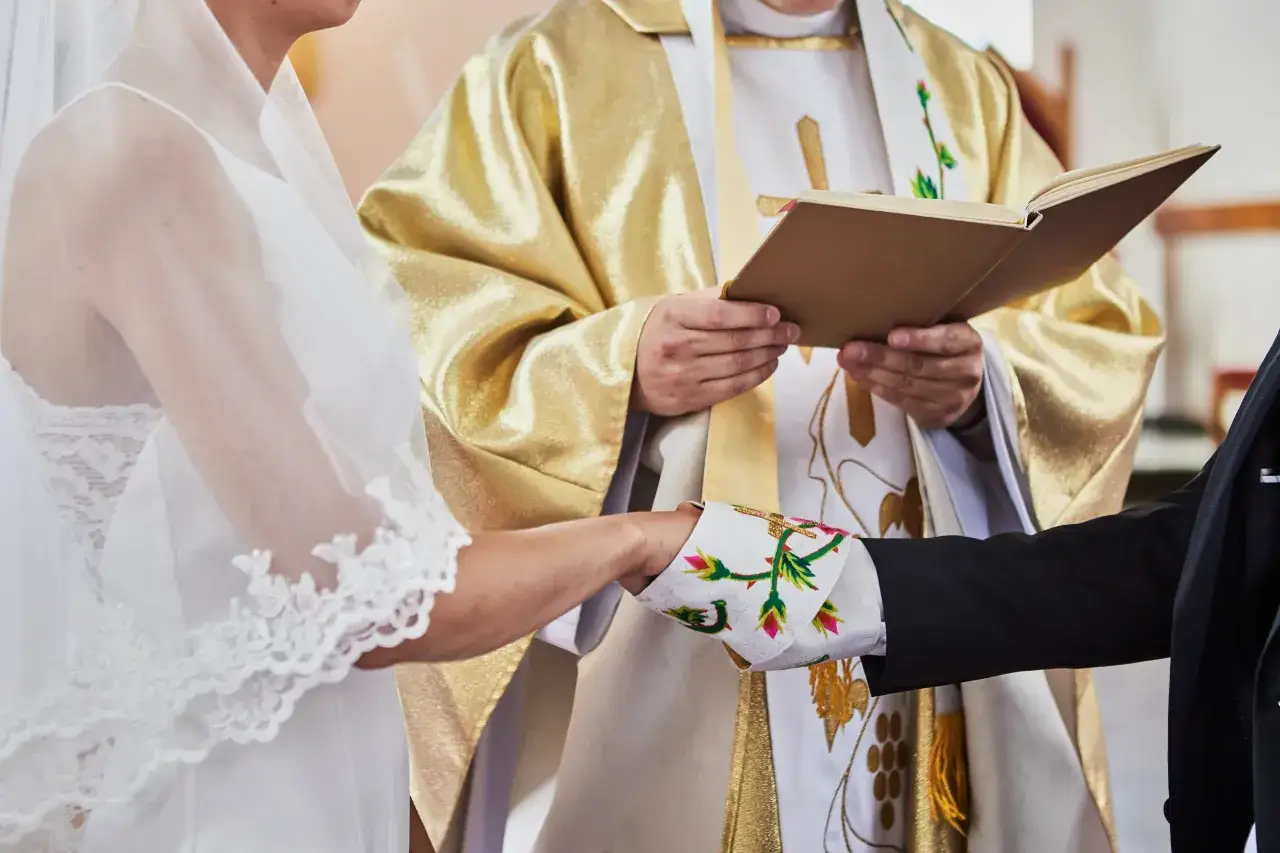 Para młoda trzyma się za ręce podczas ceremonii ślubnej, ksiądz czyta z księgi, udzielając błogosławieństwa, jak współżyć bez grzechu.