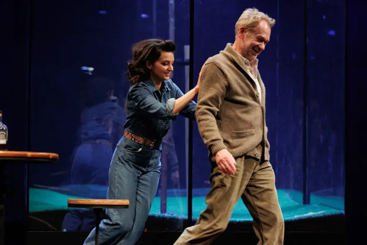 Aktorka w dżinsowej kurtce i spodniach kładzie dłoń na ramieniu starszego mężczyzny. Scena z edukacja rity spektakl.