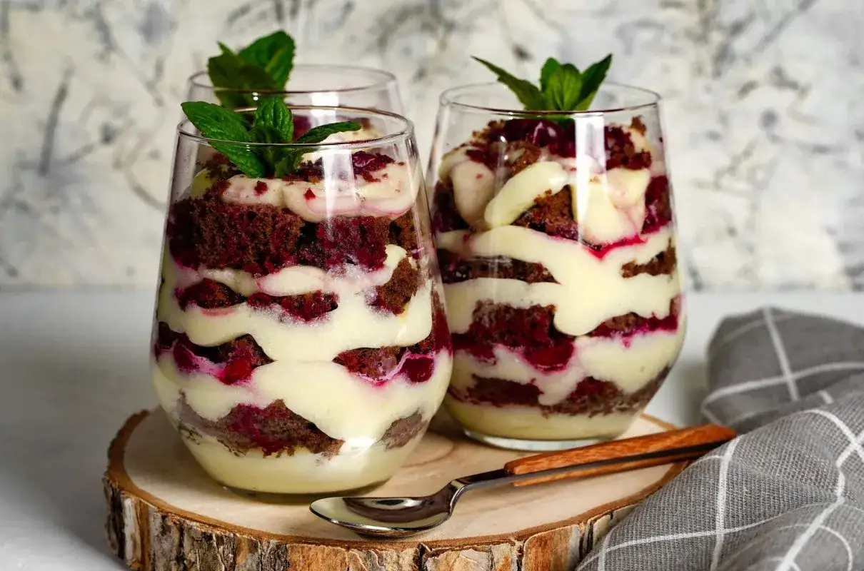 Warstwowy deser w szklance z ciemnym ciastem, wiśniami i kremem z mleka skondensowanego i mascarpone, ozdobiony miętą.