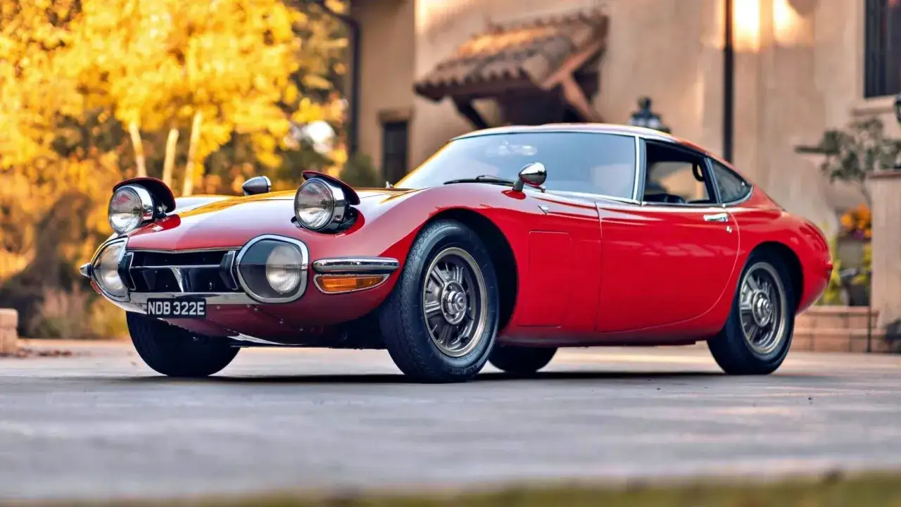 Klasyczny, czerwony Toyota 2000GT, jeden z najbardziej ikonicznych japońskich samochodów sportowych, lśni w słońcu.