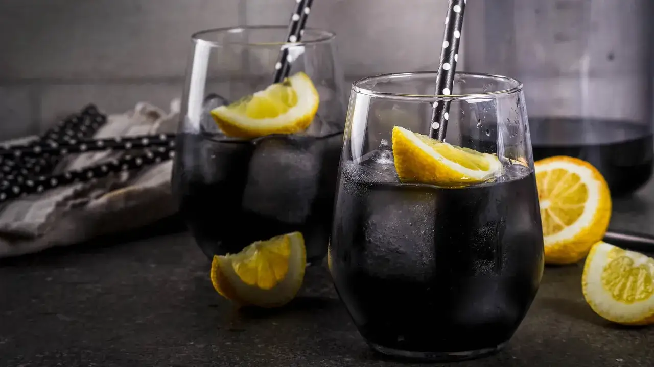 Dwa czarne napoje z lodem i cytryną, pokazujące, jak działa węgiel aktywny, pochłaniając wszystko.