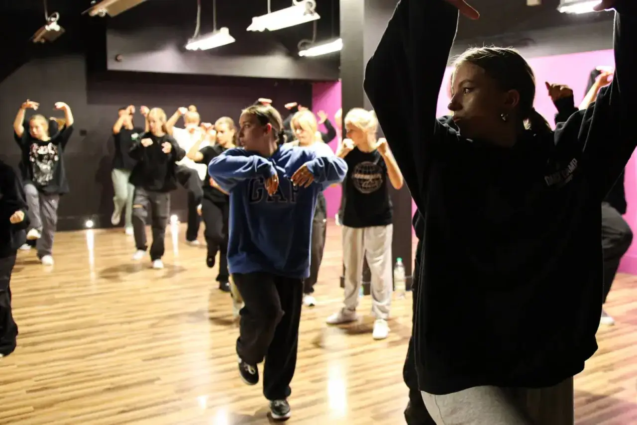 Grupa młodych ludzi ćwiczy choreografię. Widać ich zaangażowanie w naukę tańca towarzyskiego, każdy krok jest precyzyjny.