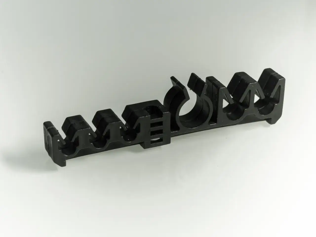 Czarny, plastikowy uchwyt z kilkoma otworami, służący do mocowania przewodów hamulcowych.